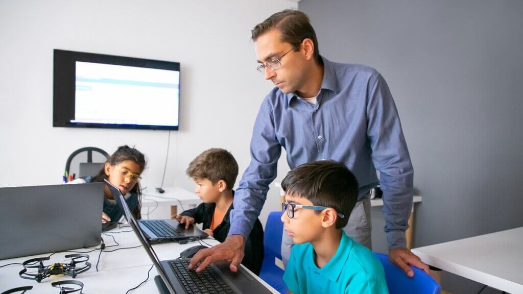 pupils doing task laptops focused teacher monitoring them